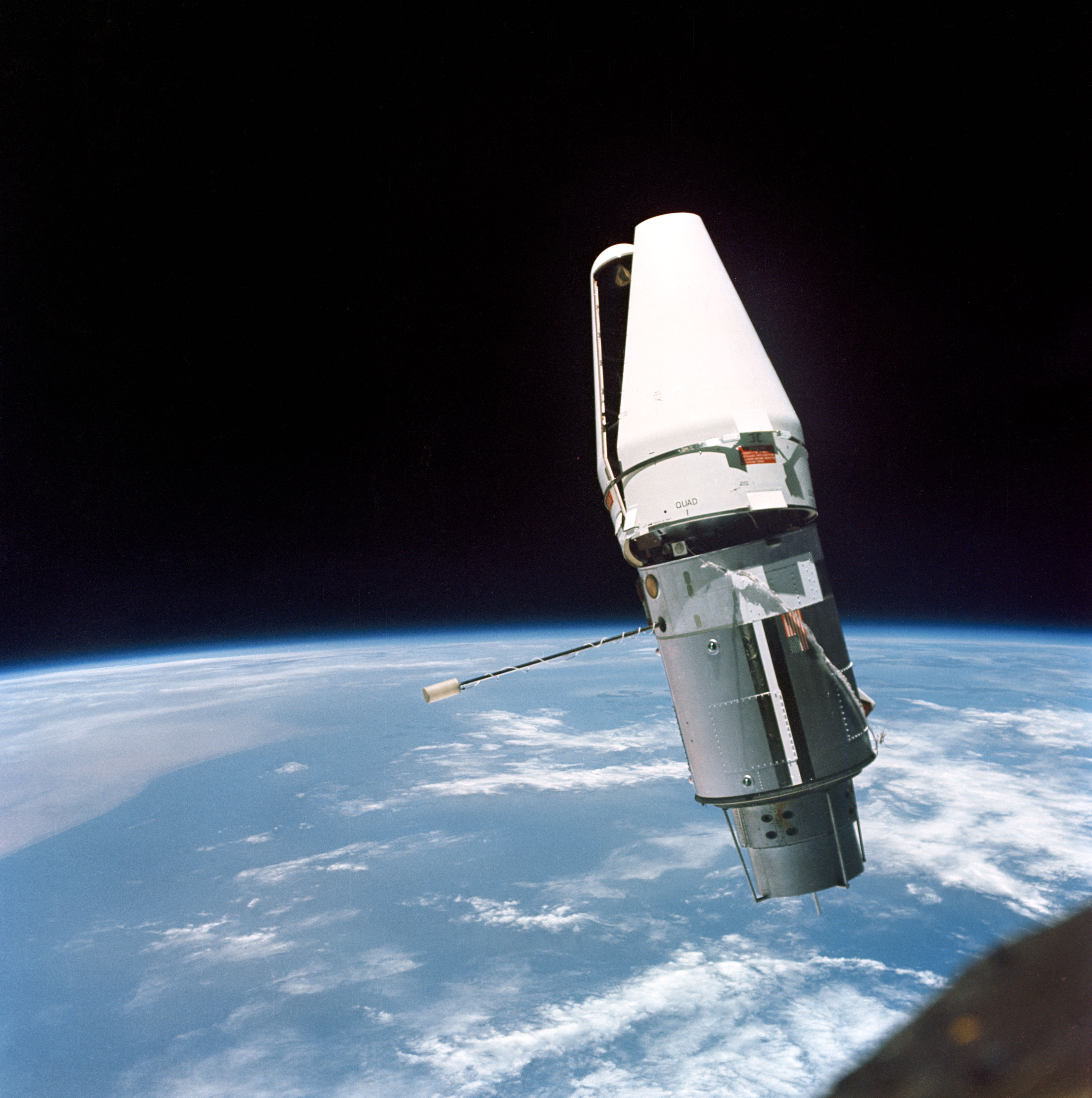 A cylindrical docking target with its white protective cover still partly attached, above Earth’s cloud-covered horizon.