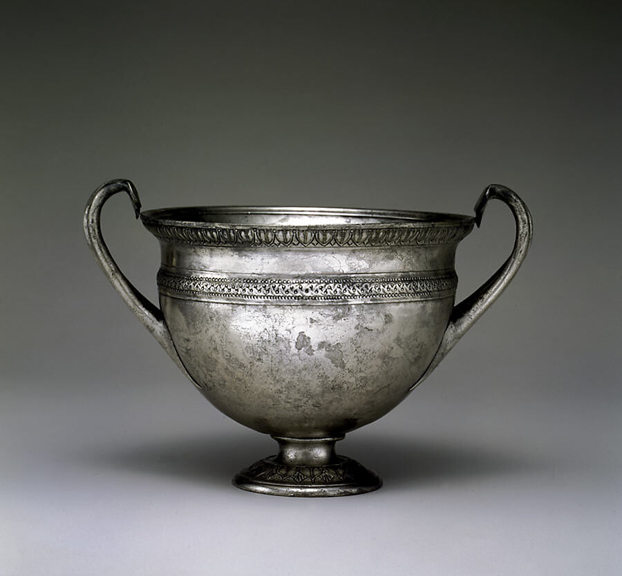 A Roman silver drinking cup has two curved handles and a short pedestal foot.