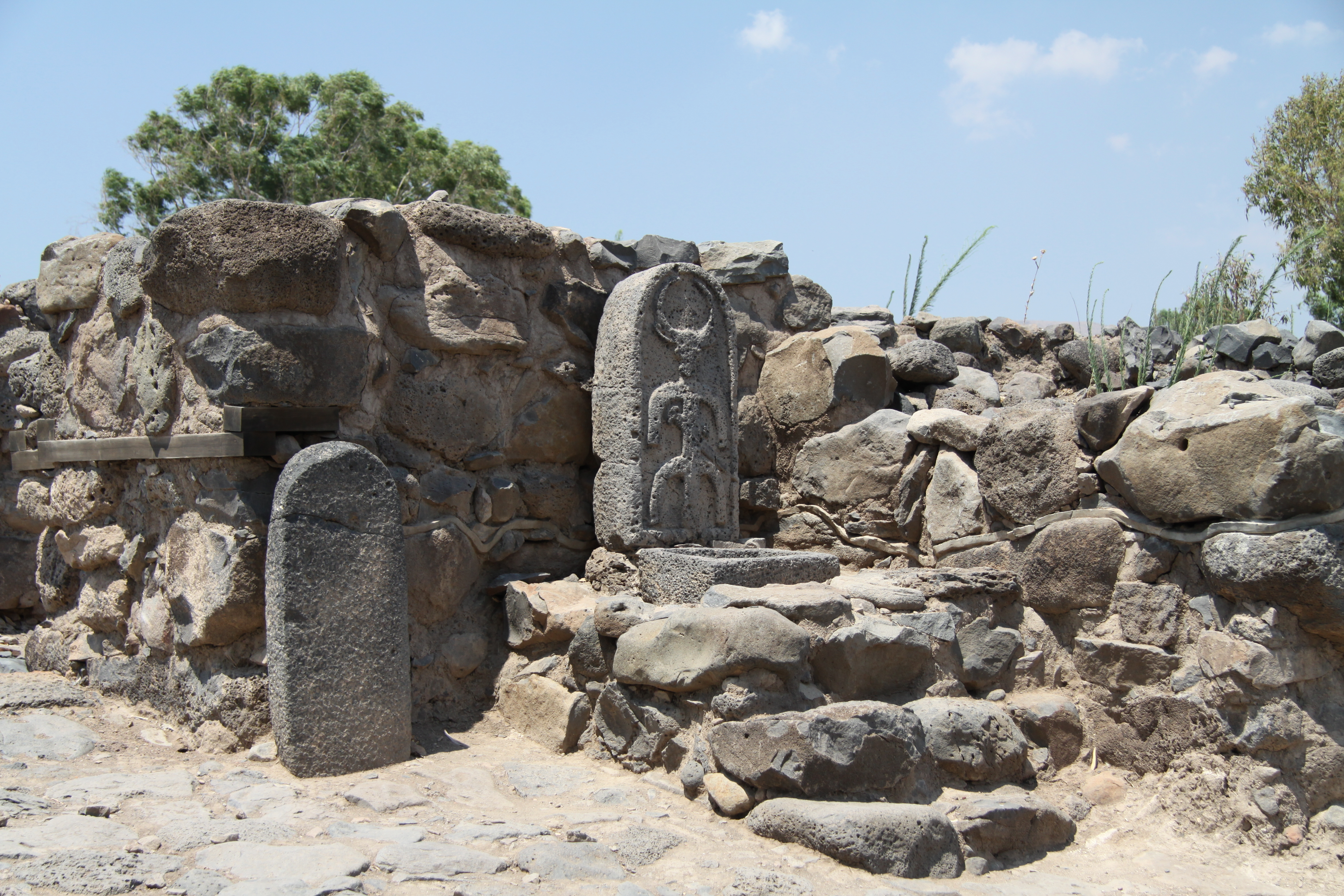 A carved upright stone stands among basalt walls in the excavated city-gate area at et-Tell.